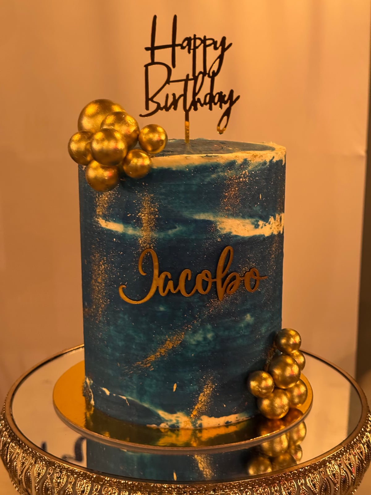Torta alta azul con pinceladas doradas, esferas y el nombre Jacobo.