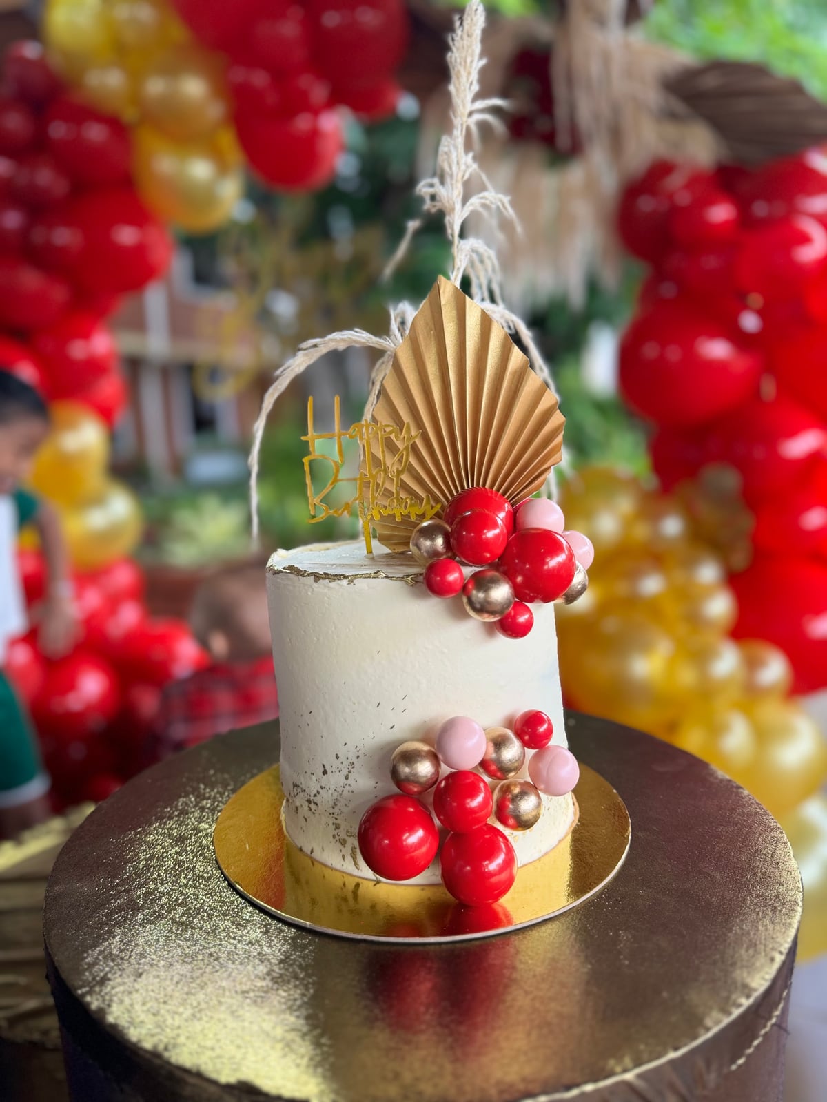 Torta blanca con esferas rojas, rosas y doradas y un abanico decorativo.