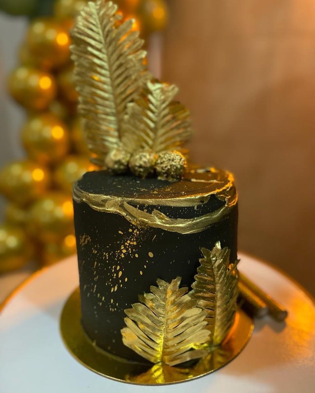 Torta negra con relieve y hojas decorativas doradas.