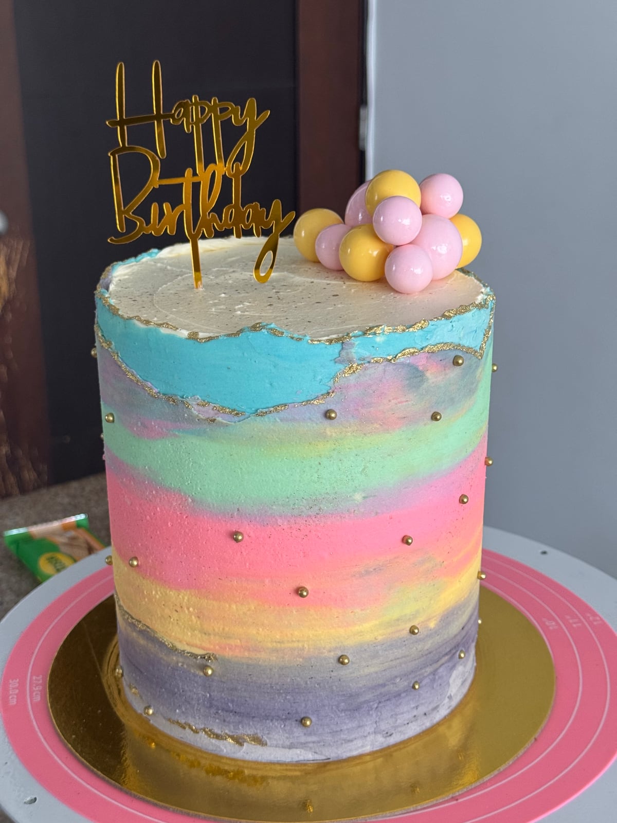 Torta alta con bandas de colores pastel, bordes dorados y esferas.